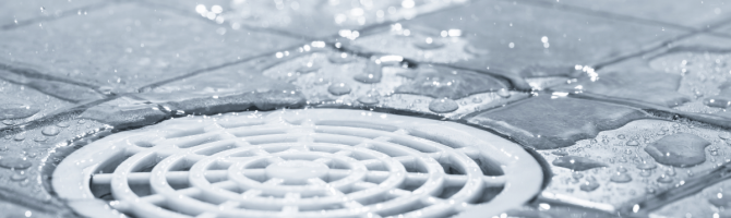 Where should the drain be placed in a shower?